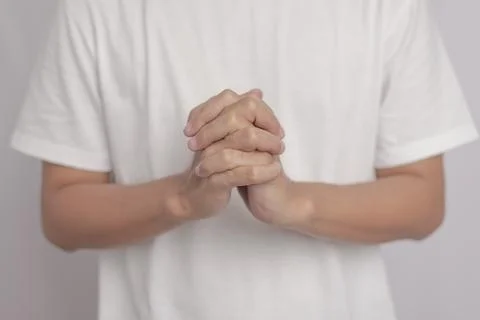 A man wearing a white shirt with both hands clasped together in a gesture t.. Stock Photos