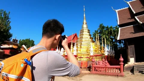 A man wearing a yellow backpack is walking in front of a red building Stock Footage 322856272