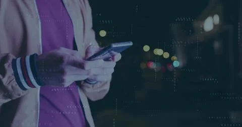 Man wearing zip-up jacket scrolling smartphone on street at night, with binary 库存照片