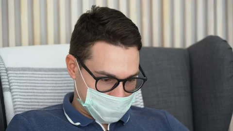 Man wears protective face mask from ARVI virus, listens to music, sits at home Stock Footage 131476679