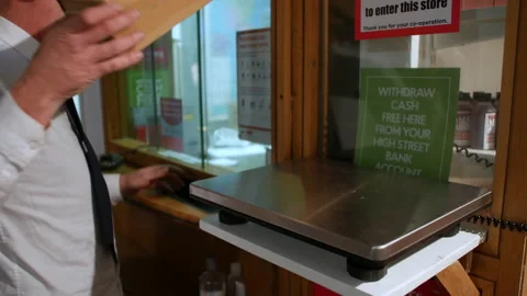 A man weighs a package parcel of electronic scales at a post office counter Stock Footage 174526499
