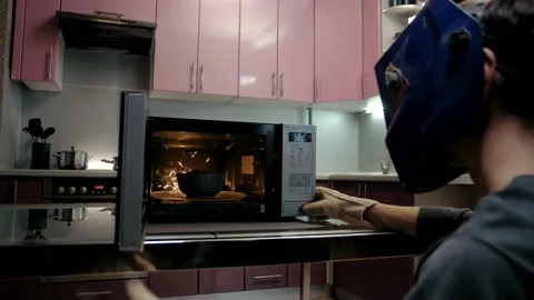 Man in a welding mask opens the microwave, which is broken Stock Footage 151646840