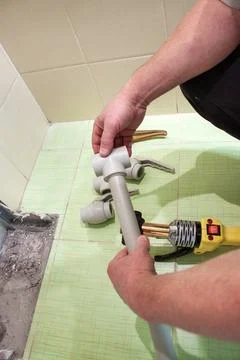 A man welding plastic polypropylene pipes with a special tool on a tiled floo Stock Photos