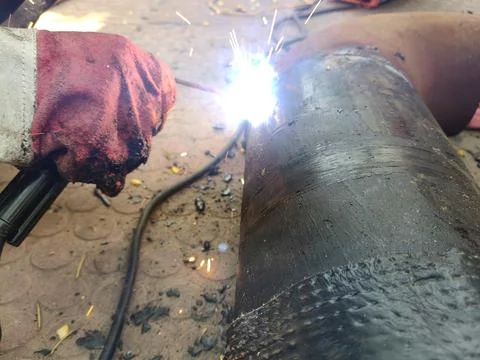 A man is welding a thick iron pipe. Stock Photos