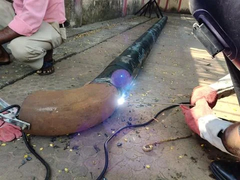 A man is welding a thick iron pipe. Stock Photos