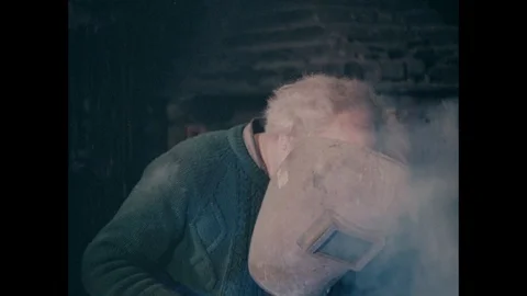 Man is welding using manual metal arc electrode wearing protective mask UK 1978 Stock Footage 132022534