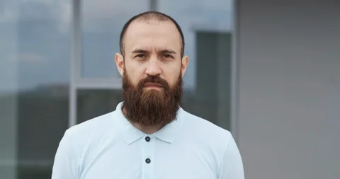Man with well-groomed beard stands on the street in front of large glass windows Stock Footage 115937372