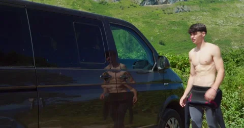 A man in a wetsuit exits a dark van, ready for a surf session Stock Footage 343671764