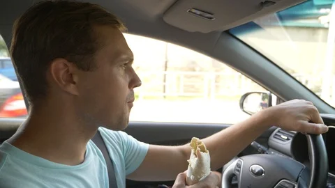 The man at the wheel of the car, eats fast food, while the car is moving. in a Stock Footage 94129044