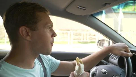 The man at the wheel of the car, eats fast food, while the car is moving. in a Foto stock