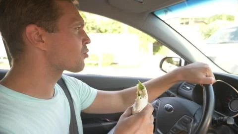 The man at the wheel of the car, eats fast food, while the car is moving. in a Stock Photos