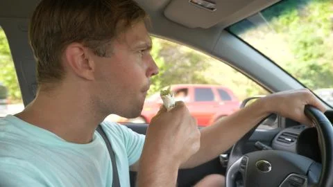 The man at the wheel of the car, eats fast food, while the car is moving. in a Foto stock