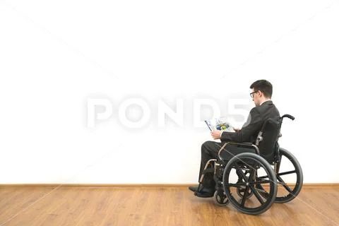 The man in a wheelchair holding papers on the white wall background Stock Photos