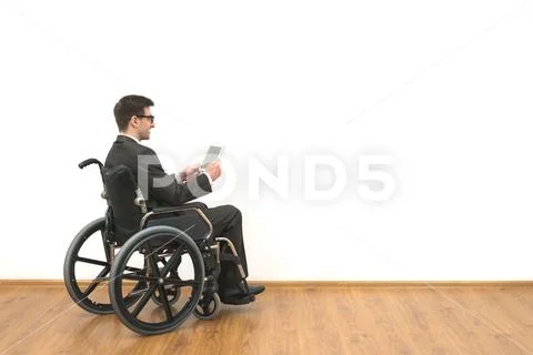 The man in the wheelchair holding a tablet on the white wall background Stock Photos