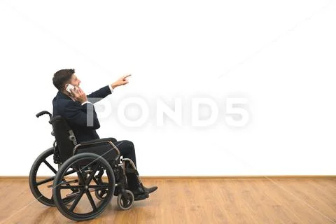 The man in a wheelchair phones and gestures on the white wall background Stock Photos