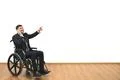 The man in a wheelchair phones and gestures on the white wall background Photo