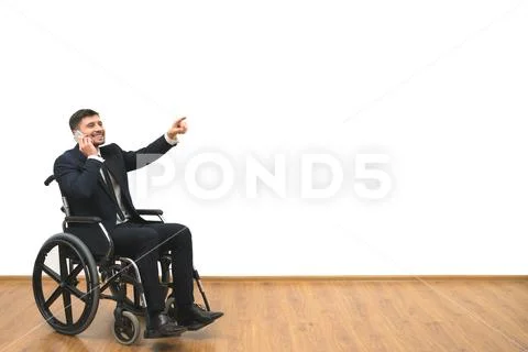 The man in a wheelchair phones and gestures on the white wall background Stock Photos