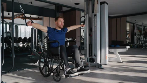 Man in wheelchair using cable machine for arm workout Stock Footage 309068250