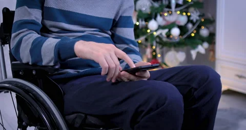 Man in wheelchair using smartphone in front of Christmas tree Stock Footage 137916692