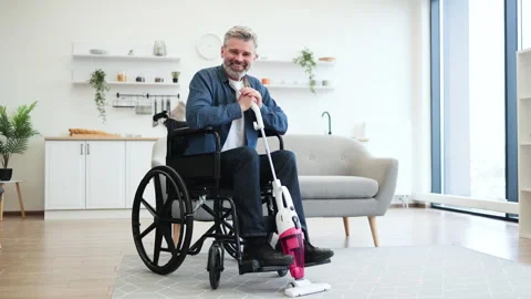 Man in wheelchair using vacuum cleaner for household cleaning work indoors Stock Footage 317290854