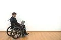 The man in a wheelchair working with a laptop on the white wall background Photo
