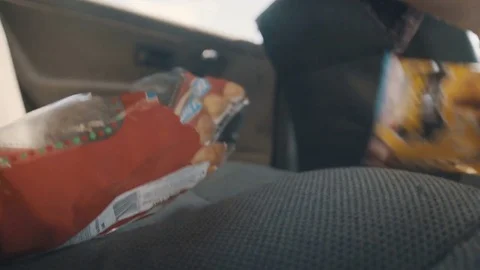 Man while driving a car grabs a snack package that's on the backseat Stock Footage 83223930