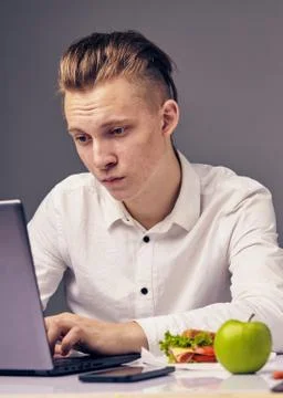 Man while lunch at the office looking at the desktop on his laptop Stock Photos