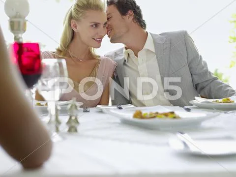 Man Whispering Into Woman's Ear At Dinner Party Stock Photos