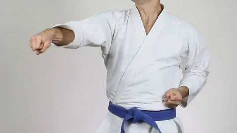 A man on a white background with a blue belt is training blows hands Stock Footage 73759947