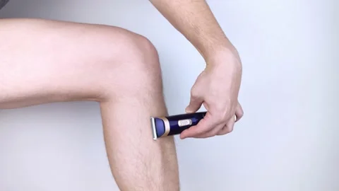 A man on a white background shaves his legs. Hairy legs and care for them. Gende Stock Footage 149025532