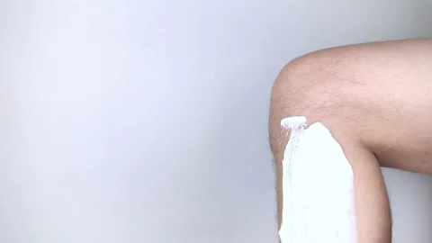 A man on a white background shaves his legs. Hairy legs and care for them. Gende Stock Footage 149025567