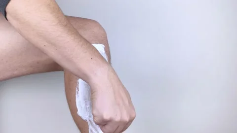 A man on a white background shaves his legs. Hairy legs and care for them. Gende Stock Footage 149025601