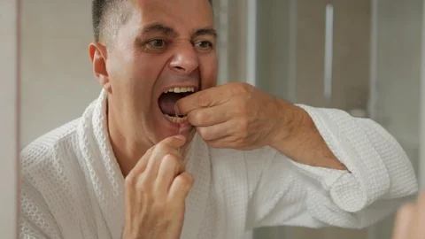 A man in a white Bathrobe standing in front of the mirror flossing his teeth Stock Footage 116500976