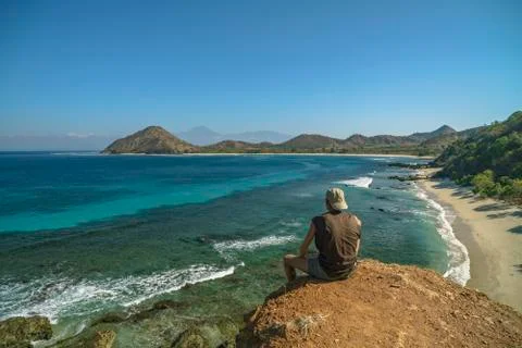 Man with a white cap is sitting at viewpoint camping location next to wild beach Stock Photos