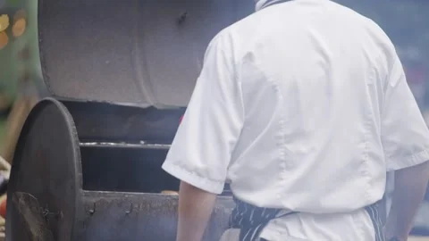 A man in a white chef's coat is standing over a grill Stock Footage 301629883