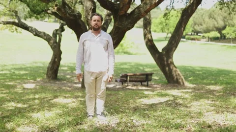 Man in white clothes doing jumping jacks in the park Stock Footage 323363192