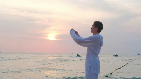 A man in white clothes stands on the beach and shoots a video on a smartphone. Stock Footage 134122676