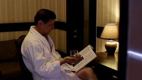 A man in a white coat, sitting at a table with reading a magazine Stock Footage 114292623