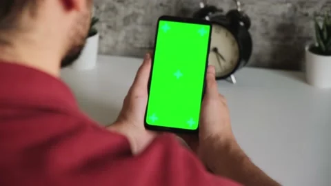 A man at a white Desk is sitting with a mobile phone in his hands with a green Stock Footage 144801840
