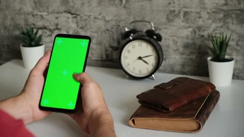 A man at a white Desk is sitting with a mobile phone in his hands with a green Stock Footage 144802113