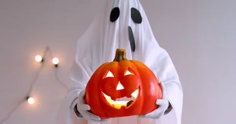 A man in a white ghost costume holds an orange pumpkin Stock Footage 279373576