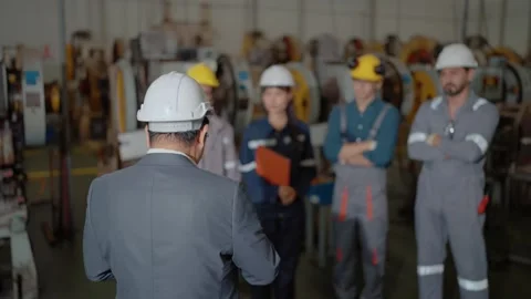 Man in white hard hat leads group in factory setting Видео 338432679
