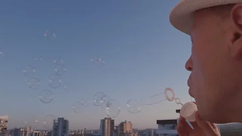 A man in a white hat blowing soap bubbles, against the sky at sunset, close-up Stock Footage 313439375