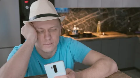 Man in white hat sits at the table uses mobile phone Stock Footage 157325265