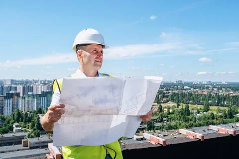 Man in a white helmet holds construction plan and inspects the construction site Stock-Fotos