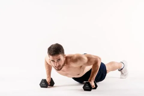 A man on a white isolated background is pushing up on the floor with dumbbell Stock Photos