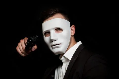 A man in a white mask on a black background, threatens with a gun Stock Photos