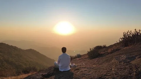 A man in white meditates in the mountains at sunset Video stock 330333386