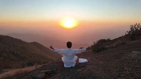 A man in white meditates in the mountains at sunset Vídeos de archivo 330333610