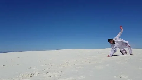 Man in White Performs Acrobatic Kick in White Sand Desert with Color Powder Stock Footage 142340421